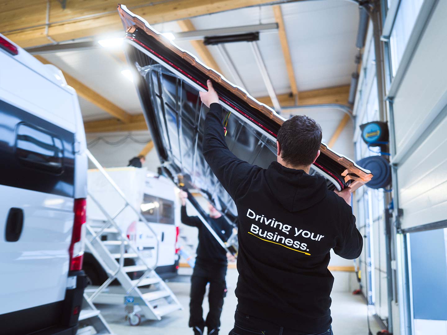 Zwei Mitarbeiter der ASB Group tragen ein großes Fahrzeugteil zu einem Campingfahrzeug