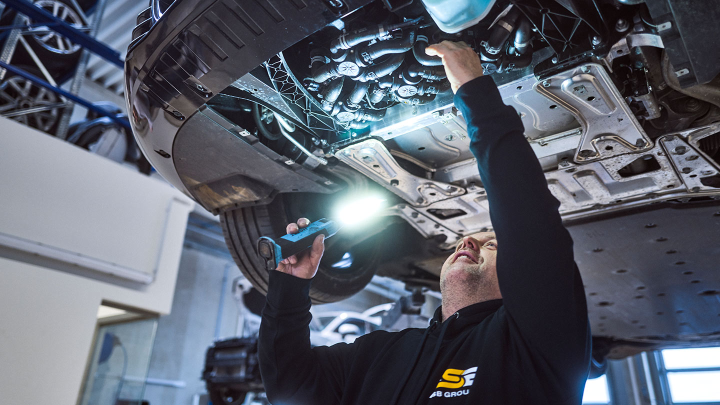 Ein KFZ-Mechatroniker der ASB Group bei der Arbeit am Unterboden eines Fahrzeugs